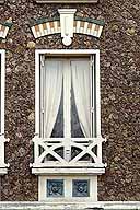 Vue d'une fenêtre avec décor de briques vernissées sur le linteau cintré et de carreaux en grès flammé sur l'allège.